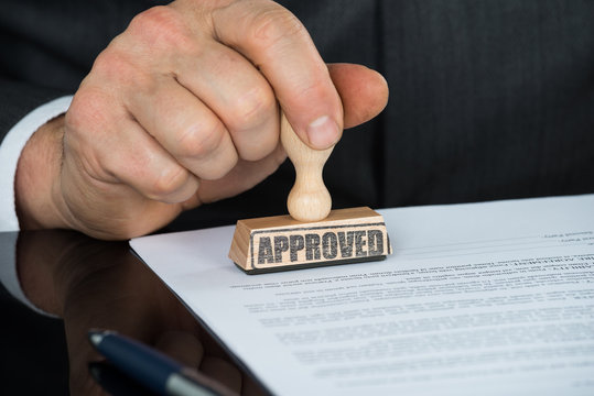 Close-up Of Businessman Hand Stamping On Approved Contract Form