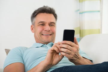 Man Lying On Sofa And Holding Smartphone