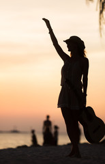 Silhouette of woman with guitar on the sunset beach