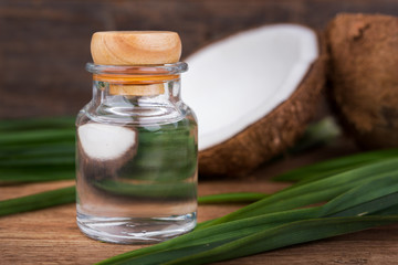 coconut oil in a bottle, background is a half of coconut and leaf on the wooden table