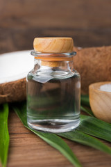 coconut oil in a bottle, background is a half of coconut and leaf on the wooden table