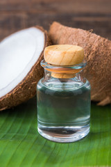 coconut oil in a bottle, background is a half of coconut on a banana leaf