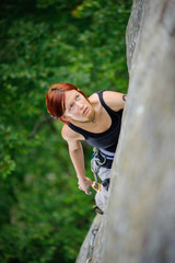 Top view of red-haired athletic female climbing steep cliff wall in summer time. Sport and Healthy lifestyle concept.