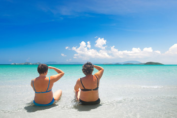 two mature woman in swimwear relaxing on the beach and enjoying