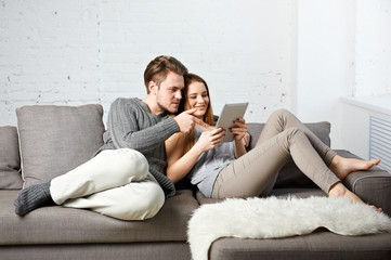 Romantic relaxed young couple using tablet computer on sofa