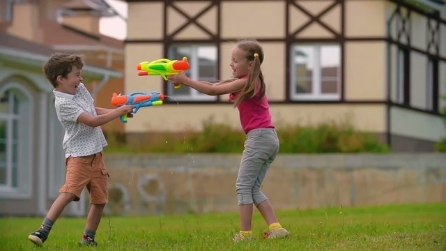 Little boy and girl playing with water guns on the green lawn near their house