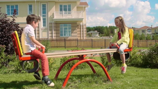 Cute girl and boy riding up and down on a seesaw on the playground