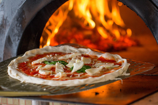 italian pizza getting in a wood burning pizza oven.