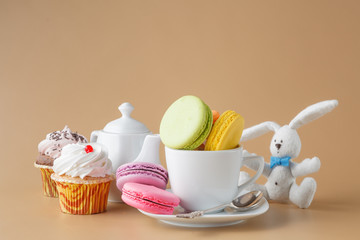 Colorful French macaroons and cup of tea on beige background