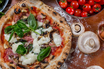 Pizza capricciosa with artichoke, ham and mushroom on wood backg