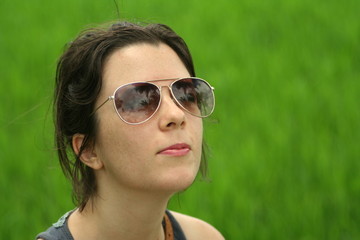 Freckled caucasian brunette girl looking up to the sun. Green grass in the background.