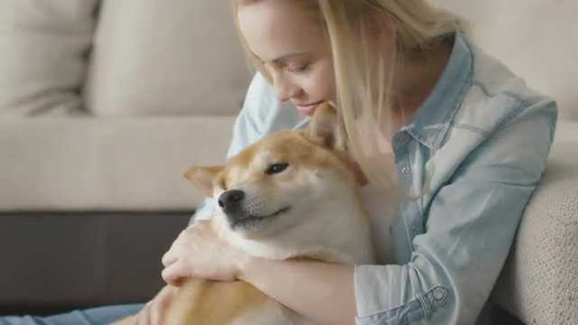 Happy blond woman is playing with pet dog at home next to a sofa. Show on RED Cinema Camera.