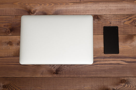 Closed Silver Laptop  And Smartphone On Brown Wooden Table