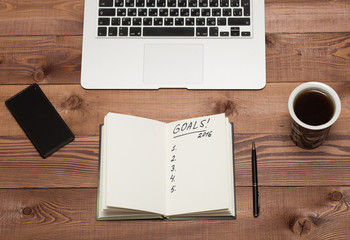 Notebook with 2016 goals, phone, laptop. coffee cup on table