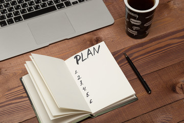 Notebook with business plan, phone, laptop. coffee cup on table