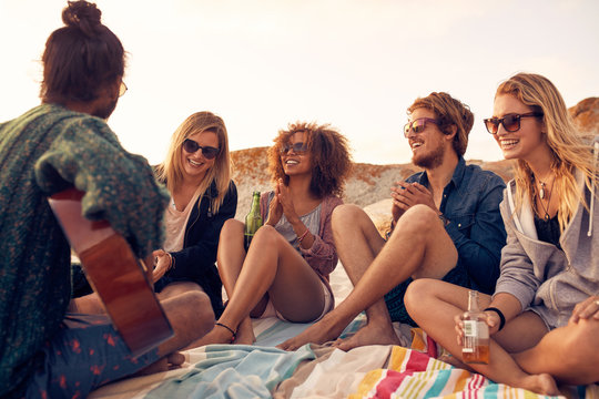 Group of people listening to friend playing guitar at the beach