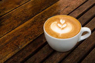 A cup of coffee with heart pattern in a white cup on wooden background.Close up