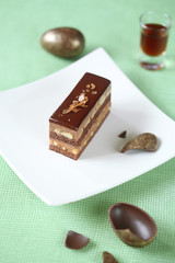 Piece of Chocolate Ester Cake served on a square white plate and broken chocolate eggs, on a light green background.