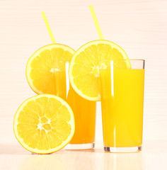 Fresh orange lemonade or juice in a glass next to the whole fruit and orange slices on a light gray background