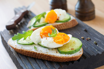 Cucumber and egg toast with arugula and cream cheese. Tasty breakfast or snack on wooden cutting...