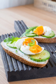 Cucumber and egg toast with arugula and cream cheese. Tasty breakfast or snack on wooden cutting board. Selective focus