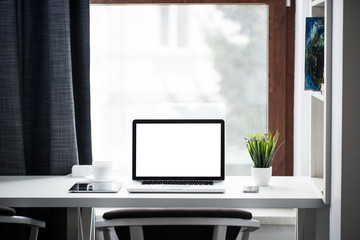 Fototapeta premium Office desk next to a window with laptop and tablet pc and a sma