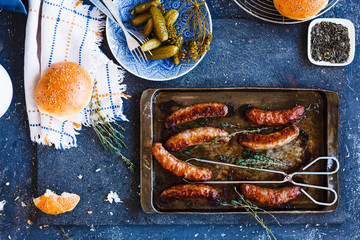 Grilled sausage pan and bread bun with cucumber pickles on a stone blue table