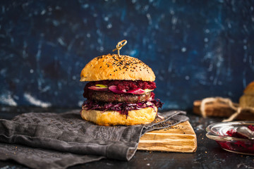 Big burger with beef cutlet, red cabbage, beetroot dip served on rustic chopping board. Rustic dark style.