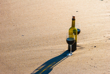 Romantic picnic with glasses of red wine sitting on the beach at the summer sunny day. Waves and sea on the background