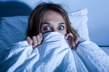 femme au lit cachée sous les draps apeurée
