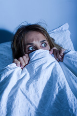 femme au lit cachée sous les draps apeurée