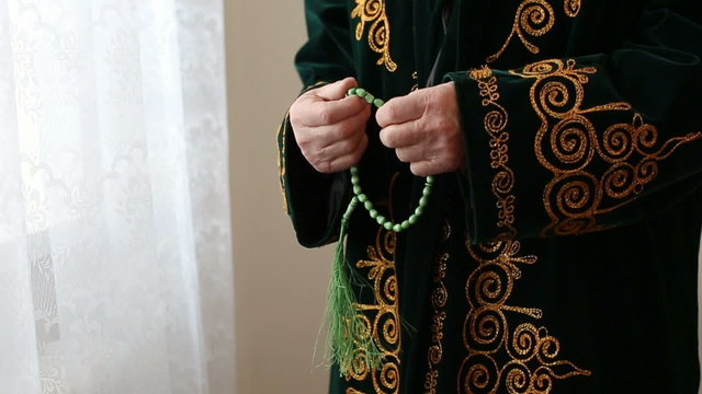 An old mullah in national dress praying with rosary beads in hands. Slow motion