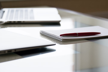 Laptop computers with notepad and pan on glass desk in office