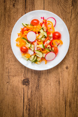 Salad with cherry tomatoes, sweet peppers, cucumbers and radishes on a wooden background