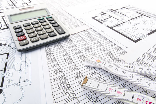 Taschenrechner und Zollstock auf Tabellen und Hausgrundrissen