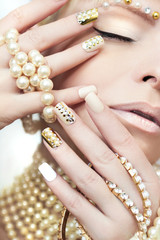 Fototapeta premium Pearl manicure with rhinestones on a gold background and pastel nails on female hand with decoration.
