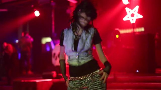 Metal dancer head banging and dancing in defocused disco background with multi color changing lights in slow motion