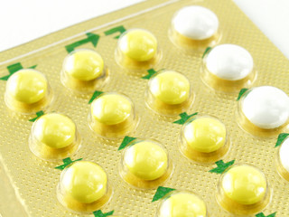 close-up yellow white oral contraceptive pills in golden aluminum blister foil packaging with green arrow instruction on white background, use of birth control pills to prevent pregnancy for women