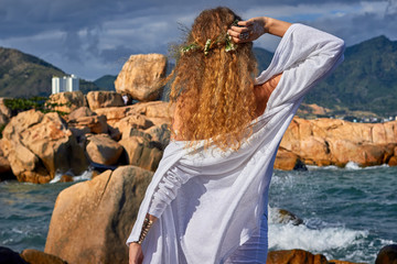  pretty curly woman  white dress standing on stone, sea view