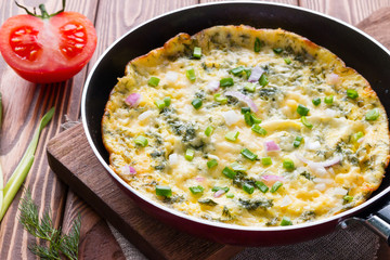 pan with a delicious omelette on a cutting board on a wooden background with vegetables