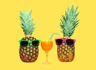 Two pineapple with sunglasses and glass fruit juice on yellow ba