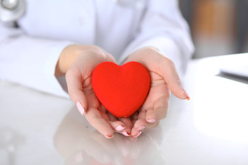 Female doctor with stethoscope holding heart.  Patients couple sitting in the background