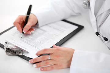 Naklejka premium Close-up of a female doctor filling out application form , sitting at the table in the hospital