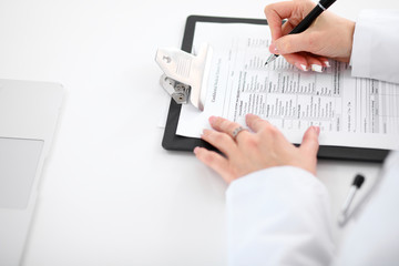 Close-up of a female doctor filling  out application form , sitting at the table in the hospital