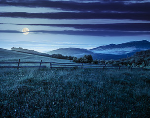 Obraz premium fence on hillside meadow in mountain at sunrise