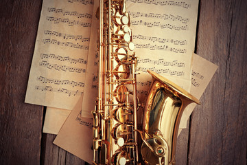 Golden saxophone with musical notes on wooden background, close up