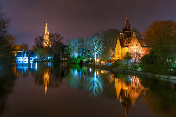 Fototapeta na wymiar Fairytale night landscape with Church of Our Lady and medieval house on Lake Minnewater in Bruges, Belgium
