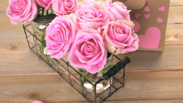 Pink roses in jars on rustic wood table
