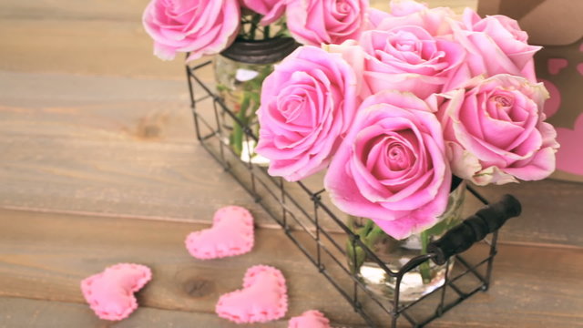 Pink roses in jars on rustic wood table.
