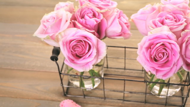 Pink roses in jars on rustic wood table.
